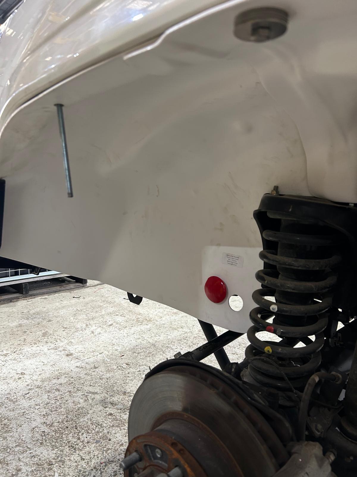 MP79S inner guard liner fitment detail showing the mounting bolt, label and coil spring in the wheel arch